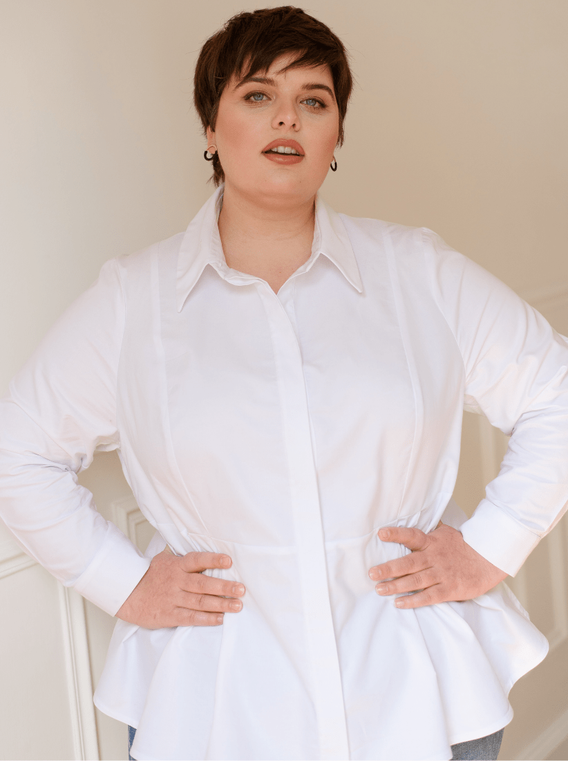 Plus-size woman wearing a white cotton shirt with a cinched waist standing with her hands on her hips